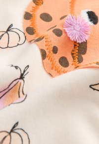 Bomuldsstof med en orange bjørn med brune prikker og en lyserød kvast, omgivet af græskarlysninger og en blød beige baggrund.