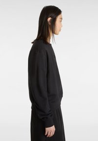 Sweatshirt noir en tissu doux, avec un col rond et des poignets côtelés. Le design est simple, sans motifs ni logos visibles.
