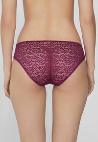 Burgunderfarbene Spitzenunterwäsche mit floralem Muster, halbtransparentem Textur und gewellten Kanten. Der figurbetonte Schnitt betont die Form.