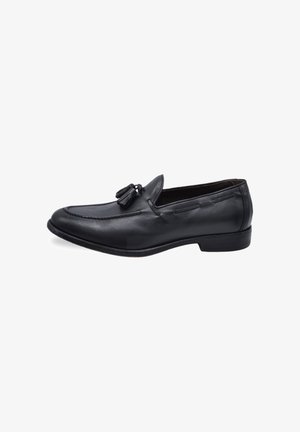 Mocasines de cuero negro con detalle de borlas, que presentan un diseño cosido y suela plana. Textura suave con una forma clásica.