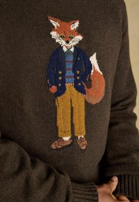 Brauner Pullover mit einem bestickten Fuchs in einem blauen Blazer, gestreifter Hemd und beigen Hosen, mit detaillierten Gesichtszügen und Pfoten.
