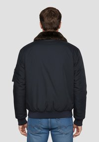 Giacca bomber blu navy con colletto in pelliccia, polsini e orlo a coste, e tasca utilitaria sulla manica sinistra. Tessuto strutturato.