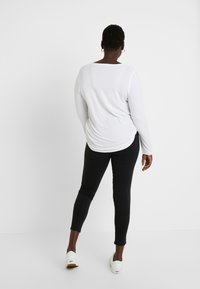 Biała bluzka z długim rękawem i okrągłym dekoltem, zestawiona z czarnymi legginsami. Całość dopełniają białe buty wsuwane.