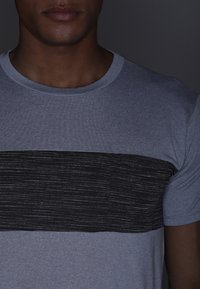 Camiseta gris con un amplio patrón de rayas horizontales negras. La tela presenta una textura suave y un diseño clásico de cuello redondo.