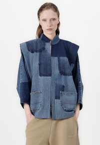 Τζιν μπουφάν με σχέδιο πατσαβούρας σε διάφορες αποχρώσεις του μπλε, με ψηλό γιακά, δύο μπροστινές τσέπες και μακριά μανίκια.