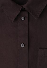 Chemise marron foncé boutonnée, col pointu, avec deux boutons visibles étiquetés "street one" et une poche poitrine à droite.
