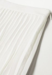 Tissu blanc plissé avec une ceinture lisse et une petite fermeture éclair sur le bord latéral.