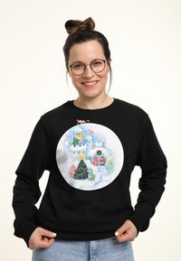 Felpa nera con una grafica circolare che presenta una scena invernale giocosa, un albero di Natale decorato e personaggi colorati in tenui toni pastello.