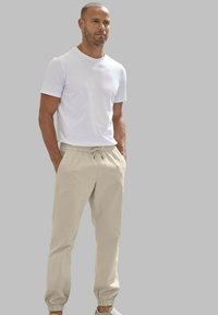 Witte t-shirt met korte mouwen, gecombineerd met beige elastische broek met enkelboorden en zijzakken. Eenvoudig, casual ontwerp.