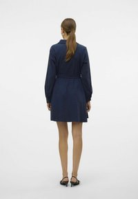 Abito camicia blu navy, con maniche lunghe e vita con cintura, presenta un colletto e arriva sopra il ginocchio. Tessuto liscio e design semplice.