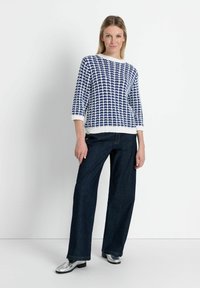 Blau-weiß gemusterter Strickpullover mit Dreiviertelärmeln, kombiniert mit dunkelblauen, weit geschnittenen Jeans und silbernen Schuhen.