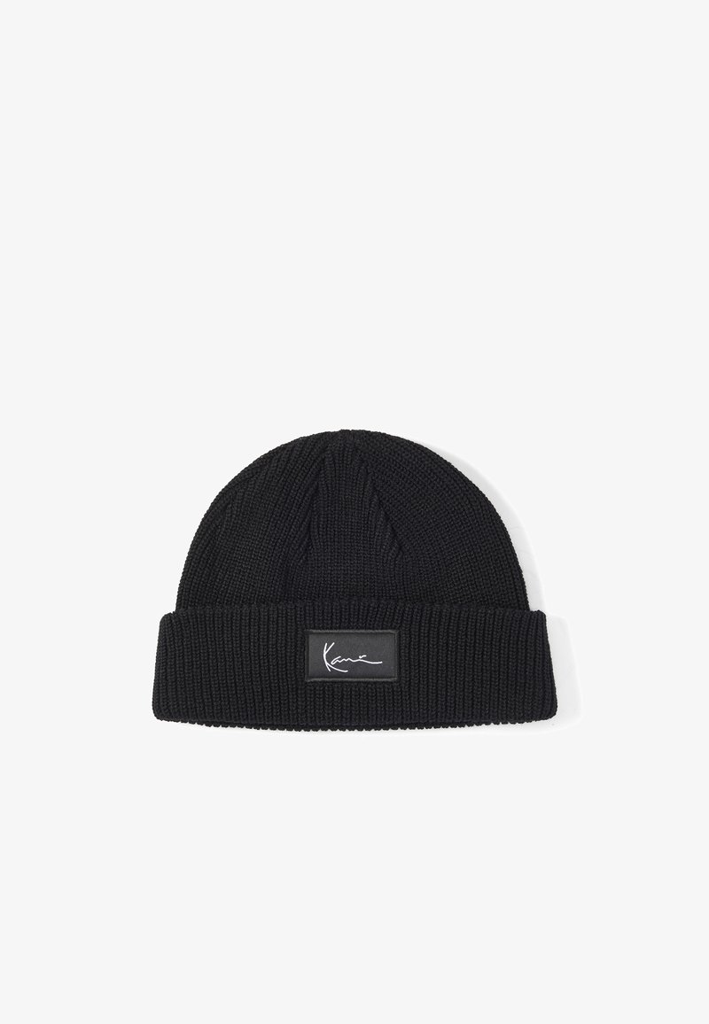 Bonnet en tricot noir avec revers plié, orné d'un patch rectangulaire portant un logo blanc dans le style d'une signature, centré sur le revers.