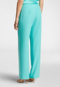 Pantaloni a gamba larga aqua realizzati in un tessuto morbido e leggero. Caratterizzati da una vita sagomata e pieghe sottili, abbinati a tacchi color cuoio.