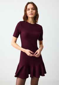 Bordeaux jurk met korte mouwen, een aansluitend bovenlijf en een uitlopende ruffle zoom. Zachte stof met een gladde textuur, geschikt voor verschillende gelegenheden.