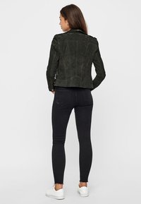 Crna antilop jakna s prilagođenim dizajnom, uparena s crnim uskim trapericama i bijelim tenisicama, prikazuje glatku teksturu i elegantnu siluetu.