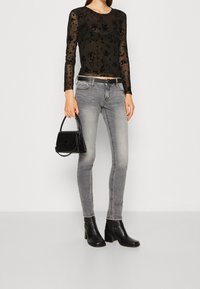 Svart mesh långärmad skjorta med blommönster, grå åtsittande jeans, svarta klackboots och en liten svart handväska med handtag.