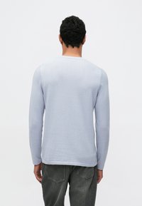 Lichtblauwe trui met lange mouwen en ronde hals, met een gladde textuur en geribbelde details aan de manchetten en zoom.