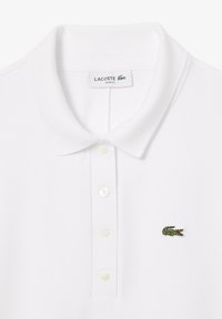 Witte polo shirt van gestructureerde katoen, met een slim fit, een klassieke kraag en een klein groen geborduurd krokodil logo. Vijf zichtbare knopen.