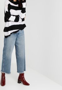 Černobíle pruhovaný pletený svetr s volným střihem, doplněný světle modrými širokými cropped džíny a lesklými burgundskými kotníkovými botami.