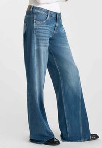 Jean en denim à jambes larges dans un bleu moyen avec un léger dégradé, présentant un design classique à cinq poches et une coupe droite.