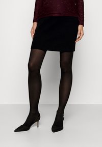 Juoda raukinėta mini sijonas derinamas su permatomomis juodomis pėdkelnėmis ir aštriakampiais slingback aukštakulniais, papuoštais akcentais.