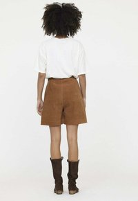 Shorts en velours côtelé marron à taille haute et jambes larges, associés à un t-shirt blanc à manches courtes et des bottes marron jusqu'aux genoux.