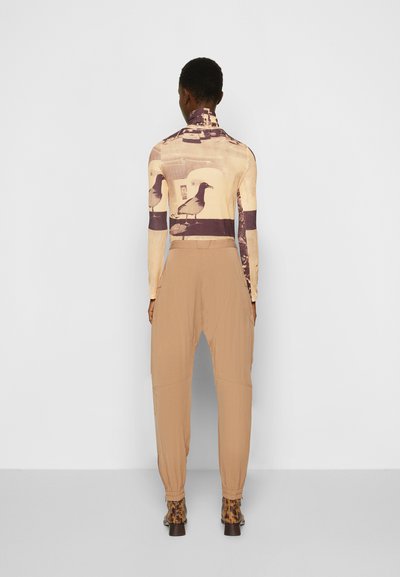 Camisola de mangas longas com uma impressão fotográfica em bege e castanho escuro; calças ajustadas em bege, com punhos elásticos; botas de tornozelo com padrão.