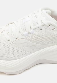 Chaussure de sport blanche avec une tige en mesh respirant, des accents texturés, une semelle rembourrée et des lacets plats pour un maintien sécurisé.