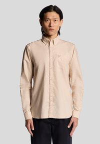 Lange mouwen, lichtbeige knoopshirt met een kraag, één borstzak en subtiele geborduurde accenten. Sportieve stoftextuur.