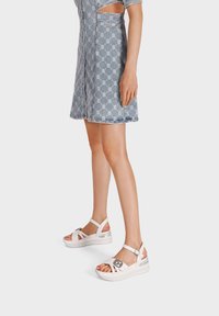 Sandali platform bianchi con fasce incrociate, dettagli argentati e chiusura a fibbia. Abbinati a un vestito di jeans blu con motivo.