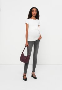 White short-sleeve top, fitted grey maternity jeans, black flat shoes with ankle straps, and a burgundy shoulder bag with a gold accent.