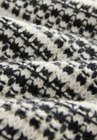 Primo piano di un tessuto lavorato a maglia in bianco e nero con un motivo a zigzag e una texture morbida e pelosa.