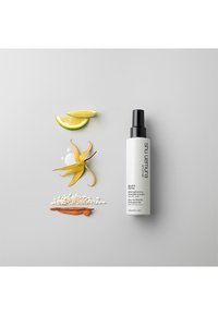 Vit sprayflaska med svart kork märkt "izumi tonic" på grå bakgrund. Åtföljs av en gul blomma, limeklyftor och spannmål.