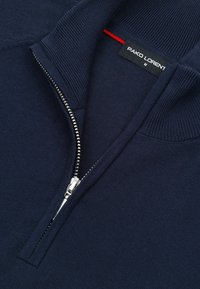 Granatowy dzianinowy sweter z srebrnym zamkiem błyskawicznym na pół, z prążkowanym kołnierzem i czarną metką marki z napisem "PAKO LORENT M."