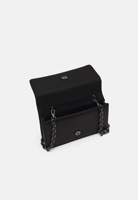 Musta suorakulmainen clutch-laukku, jossa on avattu läppä, magneettinen tuki ja lyhyt musta ketjuhihna valkoisella taustalla.