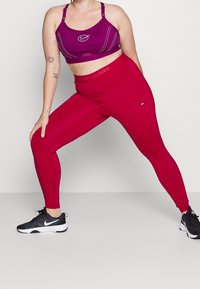 Leggings fuchsia avec une taille élastique au logo Tommy Hilfiger, associées à un soutien-gorge de sport violet avec des coutures blanches et un logo Nike. Baskets de sport noires.