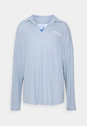 Polo bleu clair à manches longues avec un petit logo blanc "STORM" sur la poitrine et une coupe douce et décontractée.