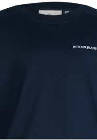 Marineblaue Baumwoll-T-Shirt mit Rundhalsausschnitt und kurzen Ärmeln, mit dem weißen Text "RETOUR JEANS", der auf der Brust gestickt ist.