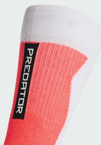 Calzino da calcio rosa acceso e bianco con materiale testurizzato. Presenta un'etichetta nera con la scritta "PREDATOR" sul lato.