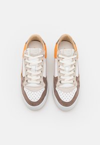 Sneakers med vit läder, mjuka bruna mockadetaljer, perforerad tå, orange häldetalj och beige snören. Modern atletisk design.