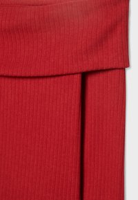 Gros plan sur un tissu côtelé rouge avec une ceinture repliée et une couture verticale, montrant la texture et les détails de la confection.