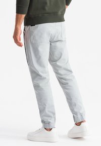 Joggers gris claro con puños elásticos, bolsillos laterales y una textura suave, combinados con zapatillas blancas. Sudadera verde neutra visible.