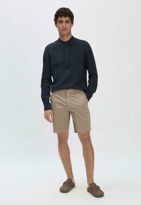 Marineblauwe longsleeve shirt met een knoopsluiting bij de kraag, gecombineerd met beige shorts en bruine instapschoenen. Eenvoudig, casual ontwerp met een aansluitende pasvorm.