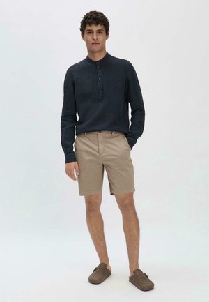 Marineblauwe longsleeve shirt met een knoopsluiting bij de kraag, gecombineerd met beige shorts en bruine instapschoenen. Eenvoudig, casual ontwerp met een aansluitende pasvorm.