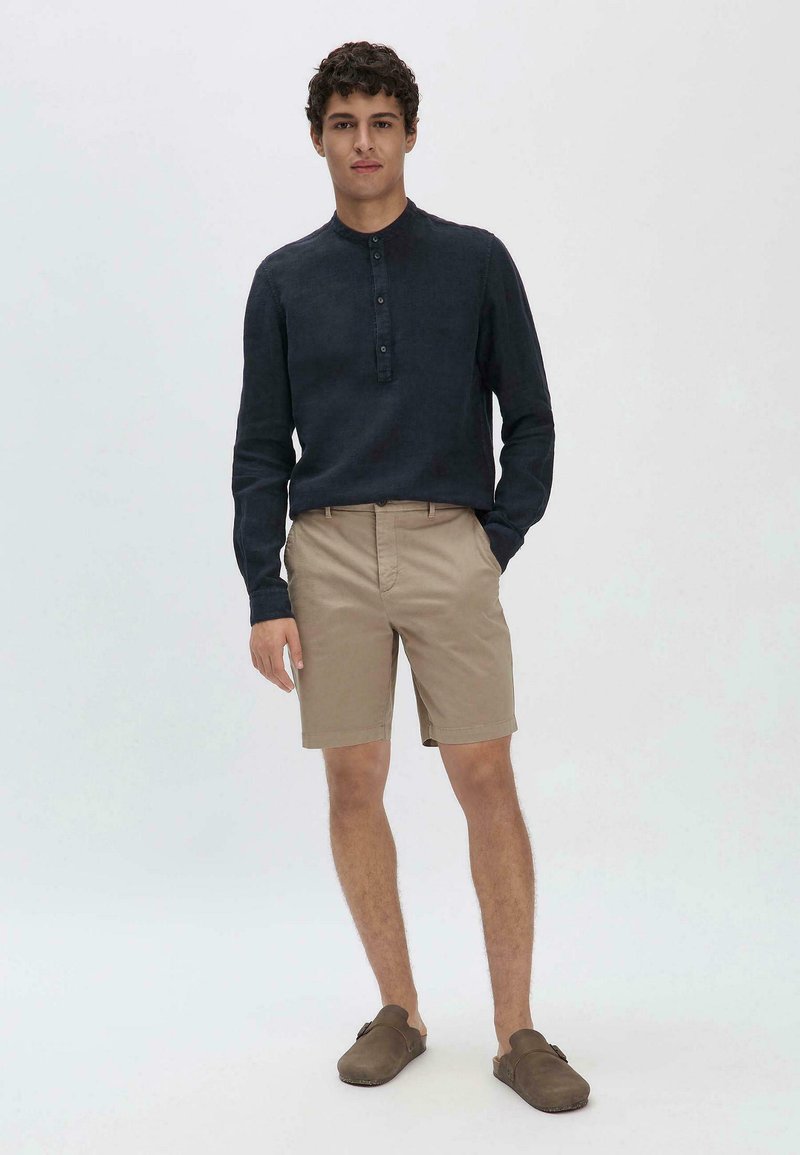 Marineblauwe longsleeve shirt met een knoopsluiting bij de kraag, gecombineerd met beige shorts en bruine instapschoenen. Eenvoudig, casual ontwerp met een aansluitende pasvorm.
