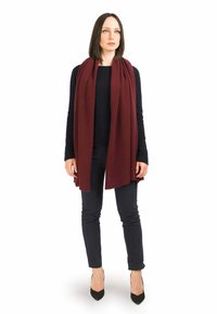 Bordeaux tørklæde lavet af blødt stof, hængende løst omkring bærerens hals. Parret med en sort sweater og slim-fit sorte bukser.