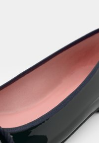 Svart patentlær ballet flatt med en glatt overflate, rosa innvendig fôr og en teksturert kant langs åpningen. Ingen synlig maskinvare.
