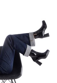 Botines de charol negro con tacones cuadrados, combinados con jeans de mezclilla oscura con puños enrollados en gris claro. Textura suave y acabado brillante.