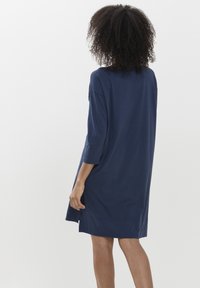 Navyblauwe, oversized jurk gemaakt van zachte stof; heeft driekwart mouwen en zijsplitten aan de onderkant voor extra bewegingsvrijheid.