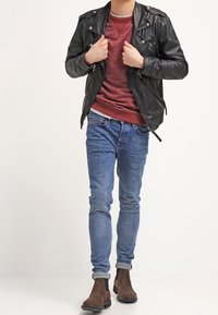 Czarna skórzana kurtka motocyklowa, bordowy sweter, niebieskie dopasowane dżinsy, brązowe botki za kostkę. Kurtka posiada zamki błyskawiczne; dżinsy mają subtelne przetarcia.